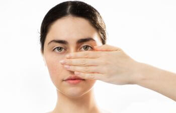Face of a sad young woman covering her nose and cheek with a hand.