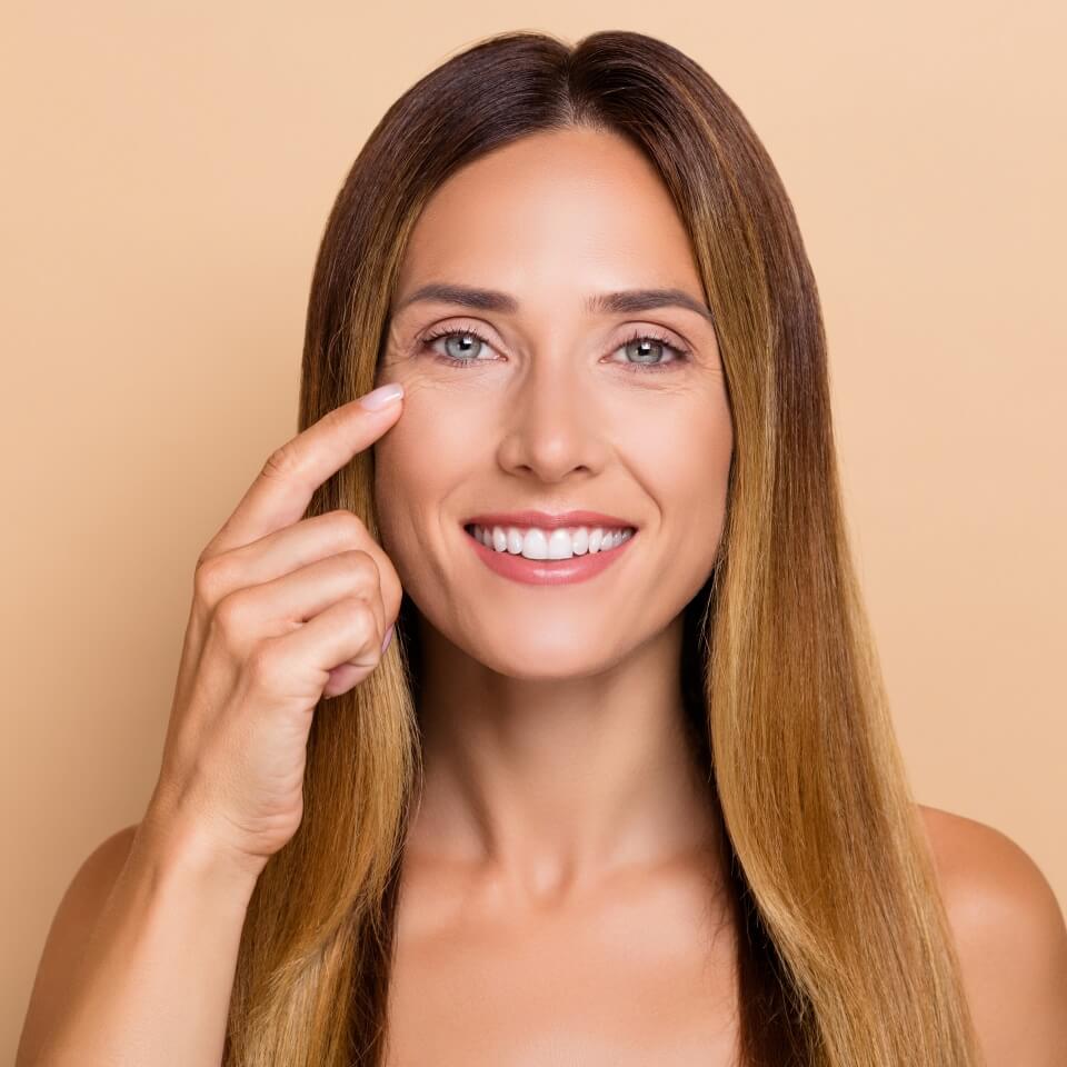 Portrait of attractive cheery woman touching under eye lifting uplift laser peeling effect isolated over beige pastel color background